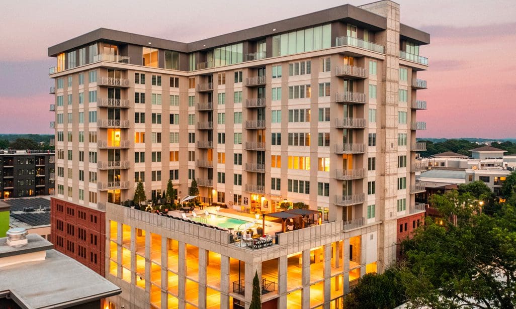 Modern apartment building with rooftop pool at sunset.