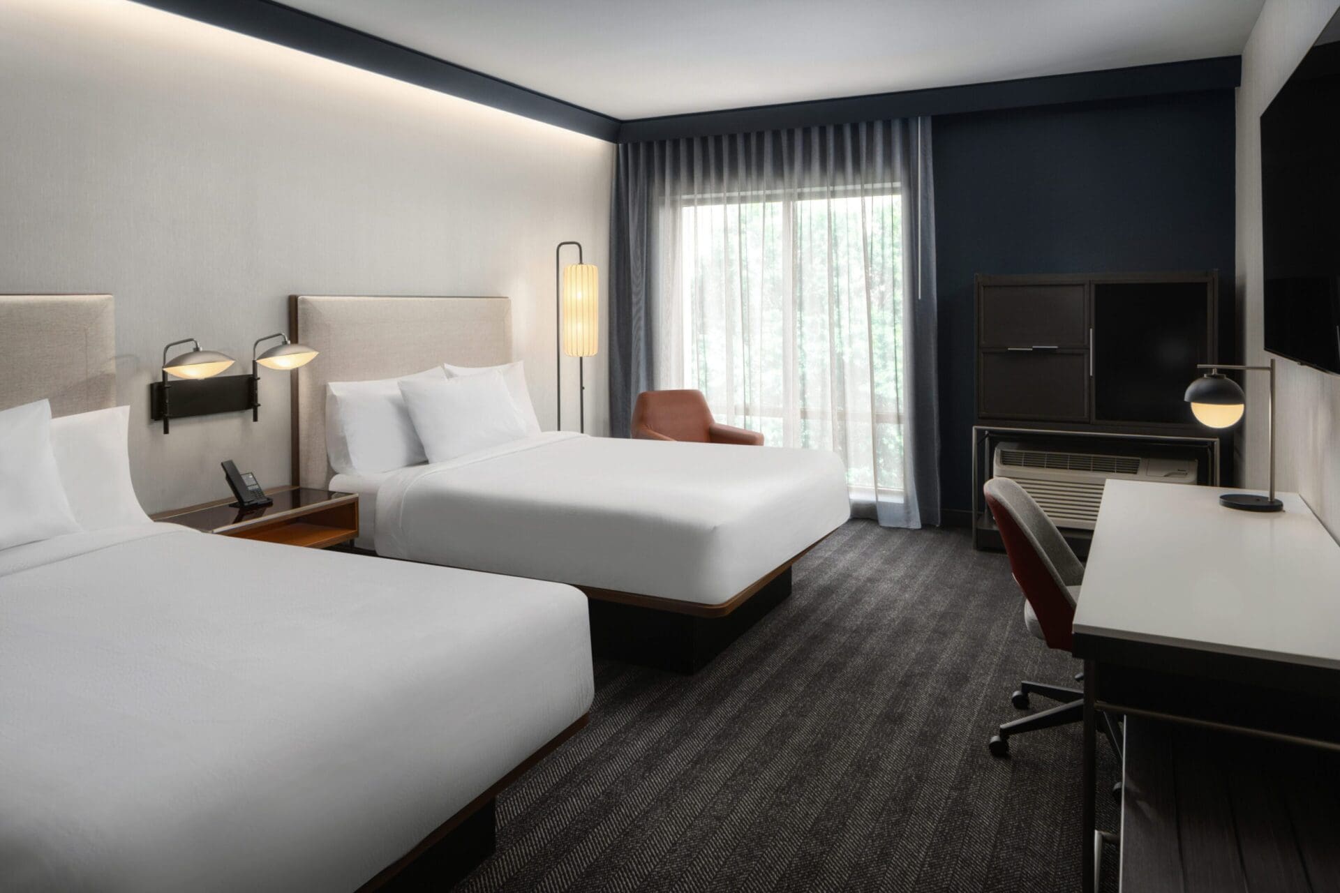 Modern hotel room with two beds, desk.