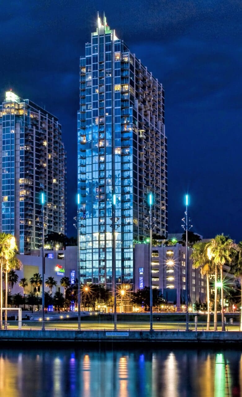 Nighttime cityscape with illuminated skyscrapers and reflections.